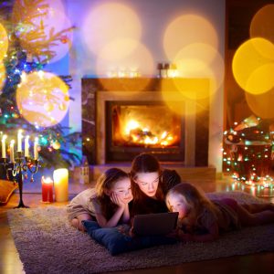 Young mother and her daughters using a tablet pc by a fireplace on warm Christmas evening
